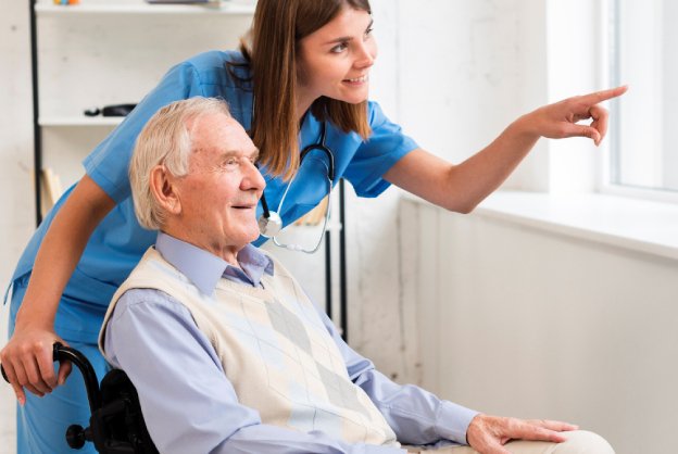 caregiver giving elder woman sitting on a wheelchair a glass of water