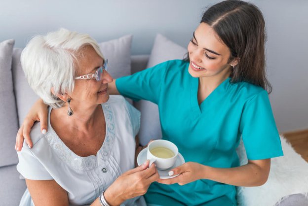 caregiver giving elder woman sitting on a wheelchair a glass of water